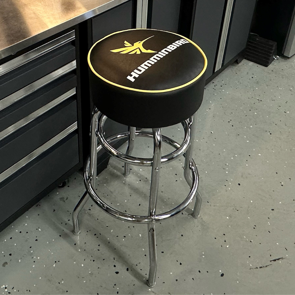 A black bar stool with a humminbird logo, set inside a workshop.