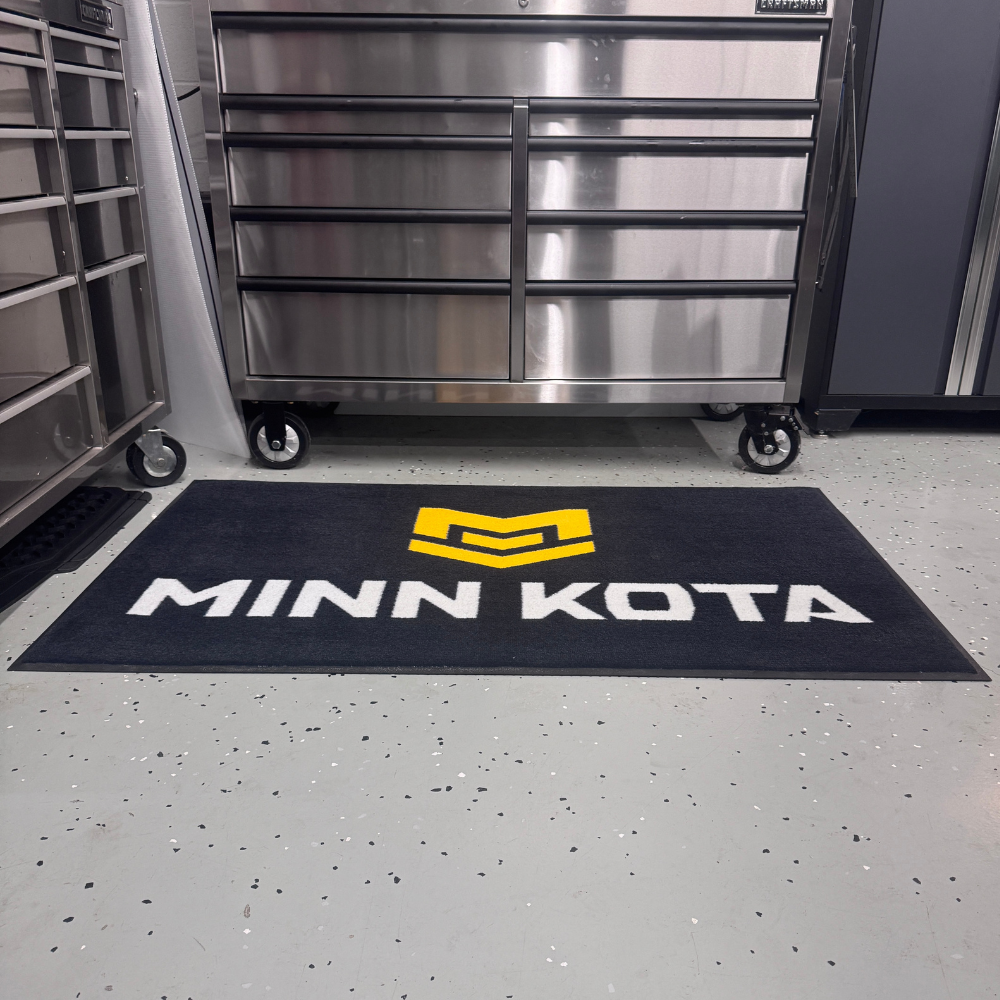 A black mat with the text 'MINN KOTA' and a yellow logo, placed on a garage floor.